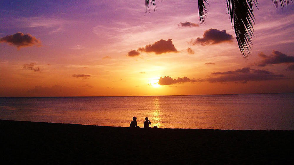 Two people watching a sunset on the coast of a tropical island